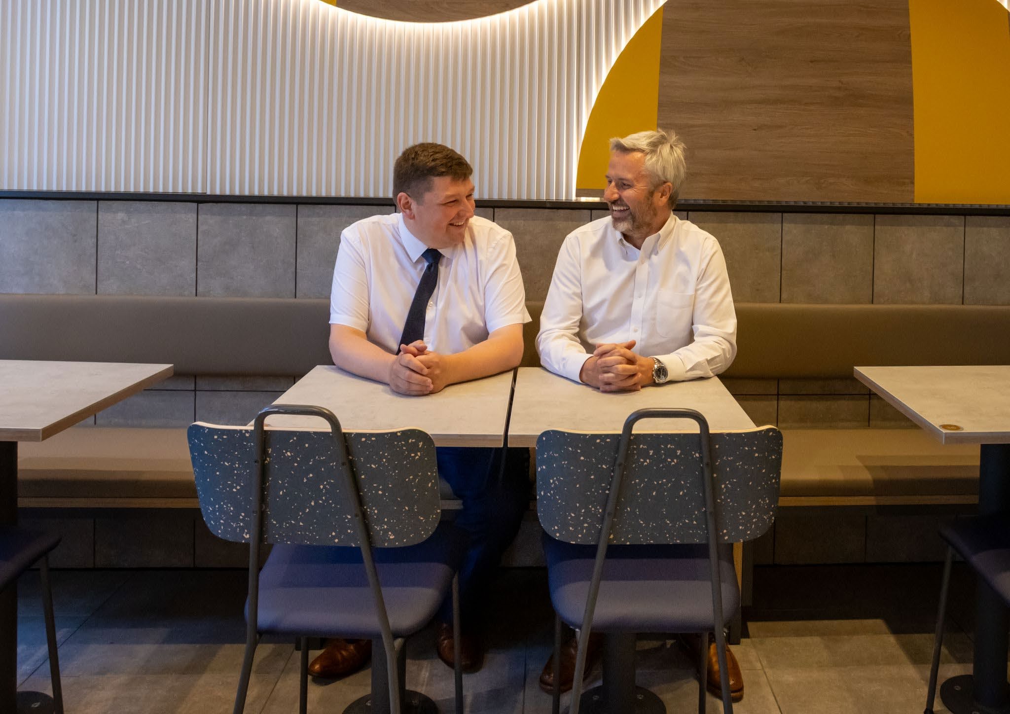 Ryan Straub and John Barr seated together at a restaurant table, with the golden arches behind them